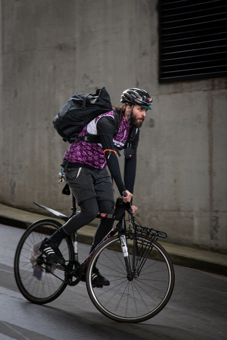 Kurierender mit Rucksack fährt mit dem Fahrrad eine Strasse entlang